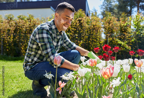 skin health, gardening and people concept - happy smiling middle-aged man with vitiligo on his face taking care of tulip flowers at summer garden © Syda Productions
