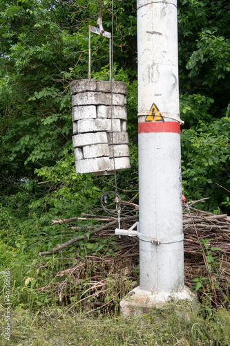 Railway power grid concrete support with adjustable counterweight against roadside bushes background