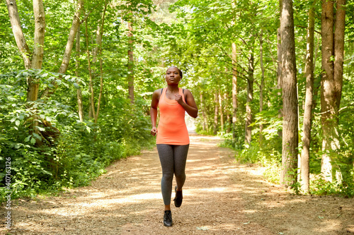 fitness, sport and healthy lifestyle concept - young african american woman running in forest