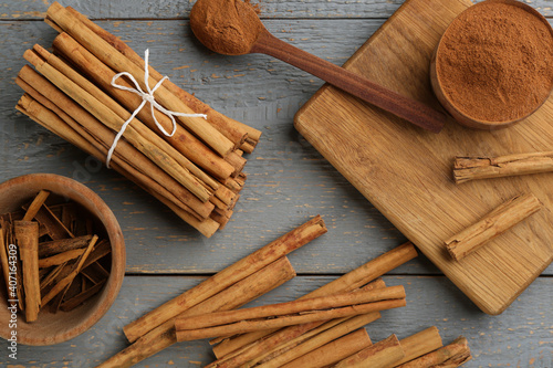 Aromatic cinnamon sticks and powder on grey wooden table, flat lay