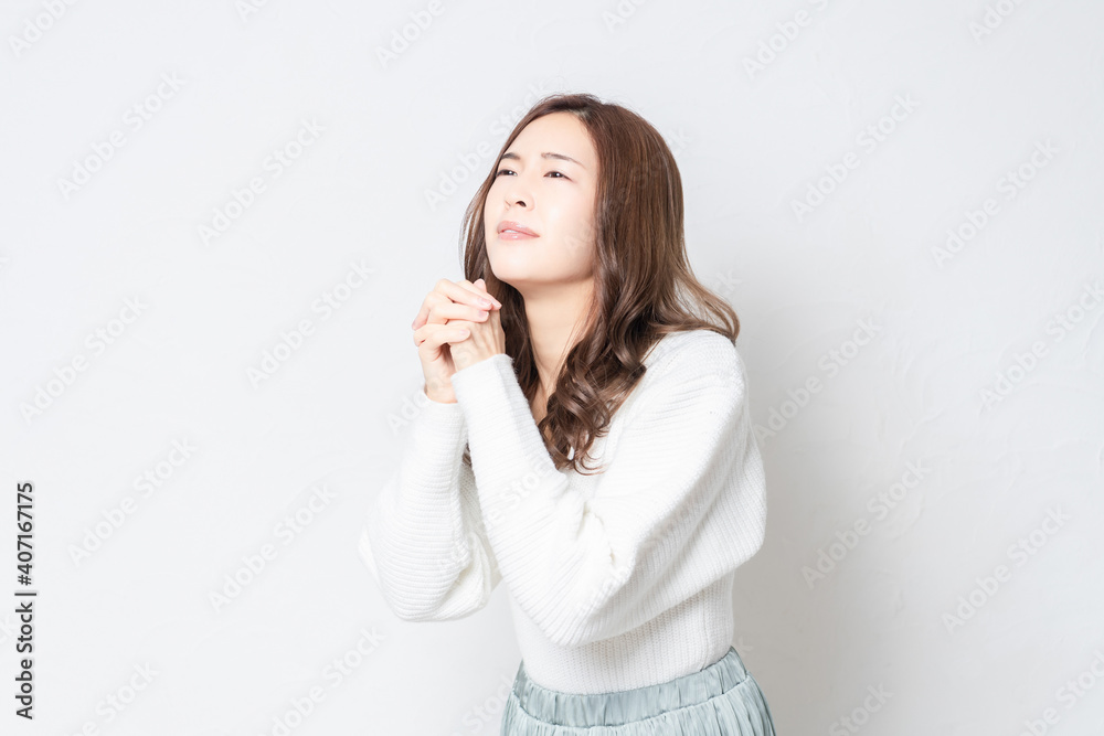 白い壁の前に立って、お願いのジェスチャーをする若い女性 白い壁の前に立って、お願いのジェスチャーをする若い女性
