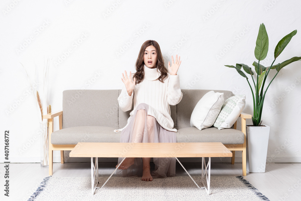 リビングのソファに座って、驚くジェスチャーをする若い女性 リビングのソファに座って、驚くジェスチャーをする若い女性