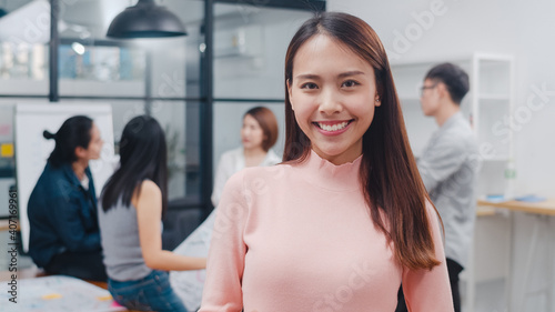 Portrait of successful beautiful executive businesswoman smart casual wear looking at camera and smiling, happy in modern office workplace. Young Asia lady standing relax in contemporary meeting room.