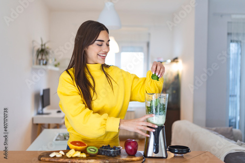 Young woman making detox smoothie at home. Girl making smoothie of fruit and vegetables. Healthy way of life. Happy girl using blender to make smoothie