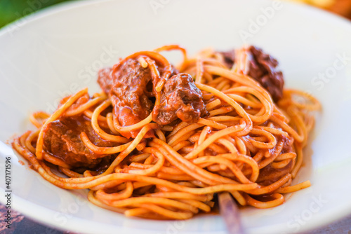 Close up kefalonian Greek spaghetti  with chunks of meat in a red bolognese sauce, outdoor eating background