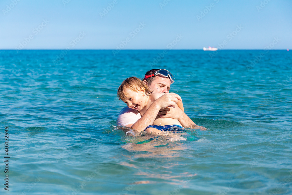 Father and little son having fun swimming and playing together in sea water at summer holidays. Family bonding, togetherness. Seaside vacation. Father and little son having fun swimming and playing together in sea water at summer holidays. Family bonding, togetherness. Seaside vacation.
