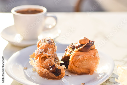 Chocolate, hazelnut and pistatio traditional greek baklava cakes served on a plate with coffee, outdoor café close upbackground