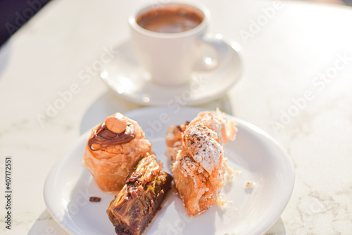 Chocolate, hazelnut and pistatio traditional greek baklava cakes served on a plate with coffee, outdoor café background