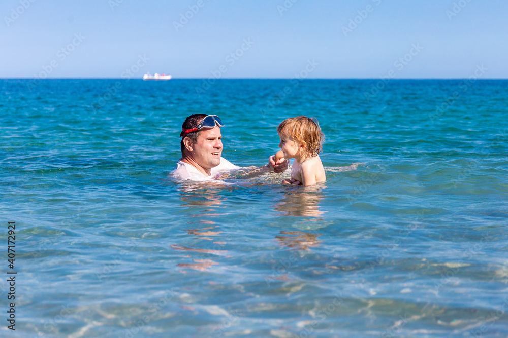 Father and little son having fun swimming and playing together in sea water at summer holidays. Family bonding, togetherness. Seaside vacation. Father and little son having fun swimming and playing together in sea water at summer holidays. Family bonding, togetherness. Seaside vacation.