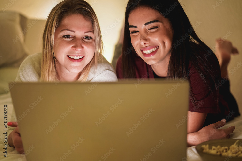 Two young girl friends using laptop computer together on bed during coronavirus lockdown isolation - Focus on left girl Two young girl friends using laptop computer together on bed during coronavirus lockdown isolation - Focus on left girl