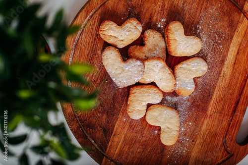 Heart-shaped cookies on round wooden cutting board. Saint Valentine's cookies in shape of heart on white background. Green leaveas and pastry. Spring freshness. photo