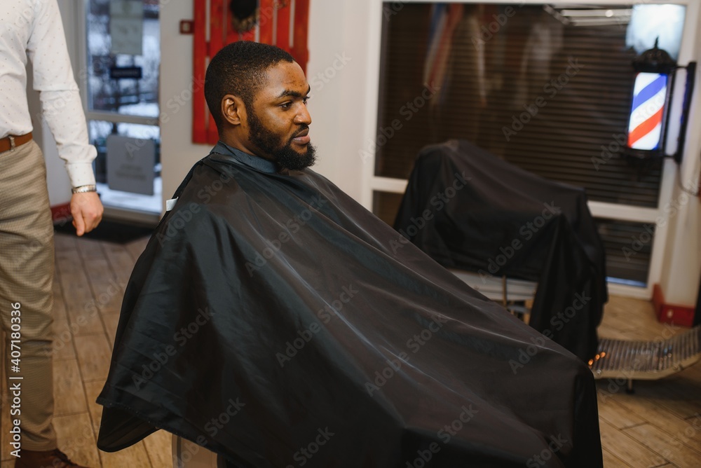Portrait of young black man being trimmed with professional electric clipper machine in barbershop.Male beauty treatment concept. Young African guy getting new haircut in barber salon Portrait of young black man being trimmed with professional electric clipper machine in barbershop.Male beauty treatment concept. Young African guy getting new haircut in barber salon