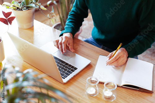 Young man learning with laptop from home or co-working space. Male freelancer connecting to internet via computer. Blogger or journalist writing new article.