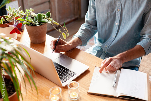 Young man learning with laptop from home or co-working space. Male freelancer connecting to internet via computer. Blogger or journalist writing new article.