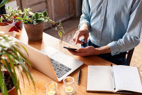 Young man with smartphone in his hands. Modern freelancer connecting to internet via computer. Blogger or journalist writing new article.
