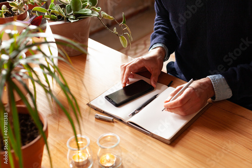 Young man writing with pen in journal. Modern freelancer connecting to internet via smartphone for a training. Blogger or journalist writing new article.