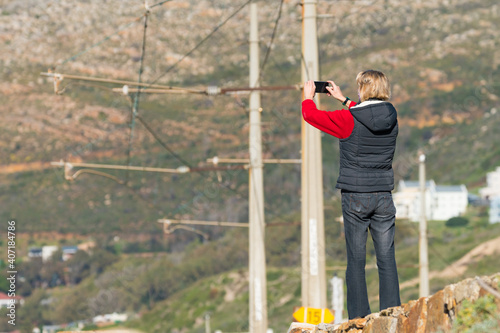 rear view of a Caucasian woman using her mobile phone to take a photo of a scene outdoors concept technology in South Africa © Childa