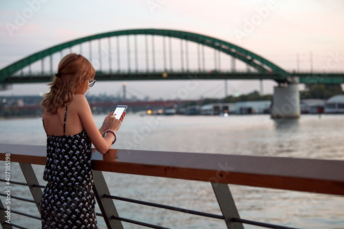 Young woman holding cellphone with blank white screen in urban city surroundings.