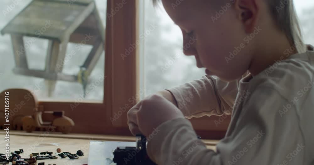 Extra close up side view of boy constructing toys from bricks slow motion. Macro shallow portrait of serious kid playing with plastic erector set indoors natural light. Children activities Extra close up side view of boy constructing toys from bricks slow motion. Macro shallow portrait of serious kid playing with plastic erector set indoors natural light. Children activities