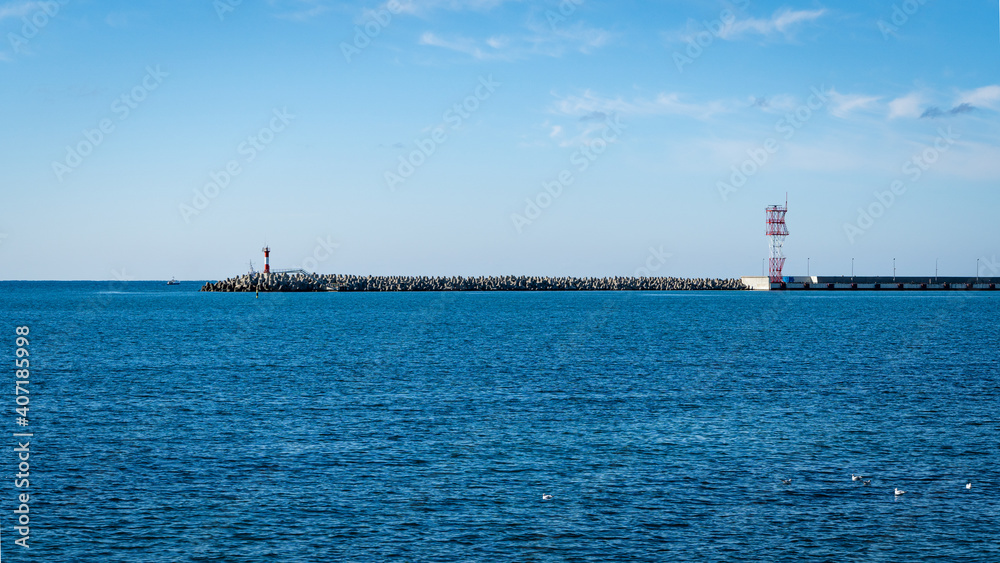 Sochi, Russia - November 25, 2020: Current city lighthouse on pier near sea station. Blue sky. Black Sea. Sunny autumn day.