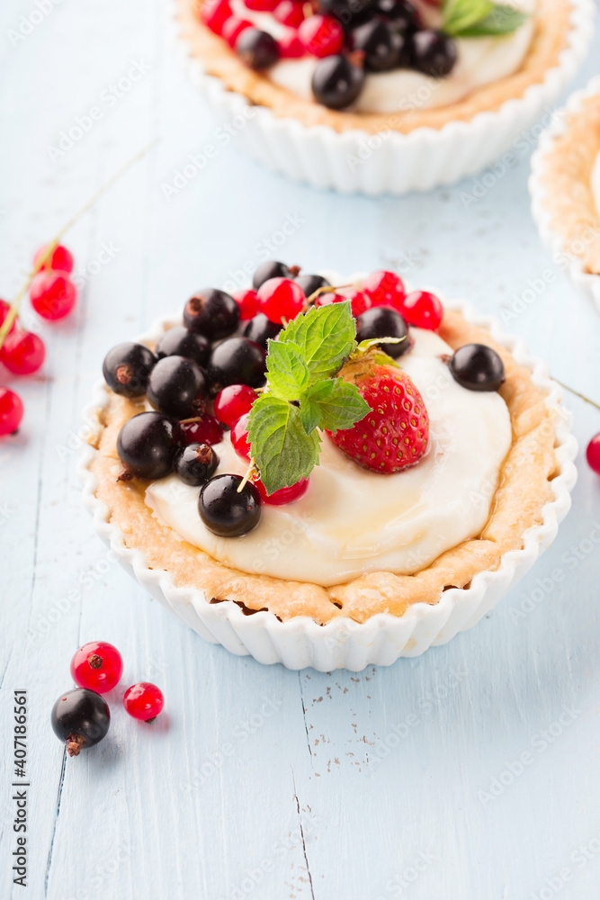 Homemade Tartlets with cream and fresh berries - ripe red and black currants, strawberries on blue rustic wooden background, top view. Homemade Tartlets with cream and fresh berries - ripe red and black currants, strawberries on blue rustic wooden background, top view.