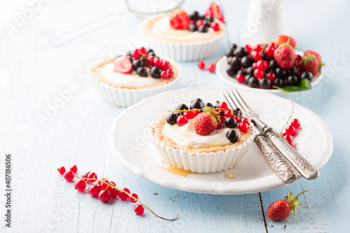 Homemade Tartlets with cream and fresh berries - ripe red and black currants, strawberries on blue rustic wooden background, top view.