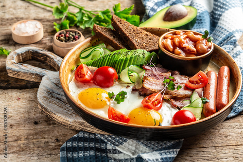 English Breakfast with fried eggs sunny side up, bacon slices, sausages, tomatoes, avocado, toasts, Nutritious morning meal. daily morning in London