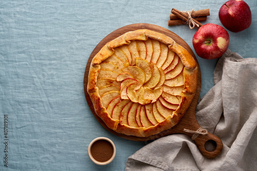 Apple pie, galette with fruits, sweet pastries on blue linen textile tablecloth, sweet crostata on cutting wooden board, side view, autumn or winter food, copy space, top view