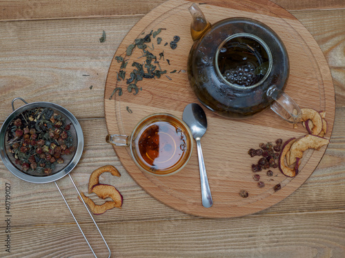Tea composition on a wooden background top view. A cup of freshly brewed aromatic black tea with mint, chamomile and dried strawberries on a wooden tray. Natural organic delicious tea in a transparent