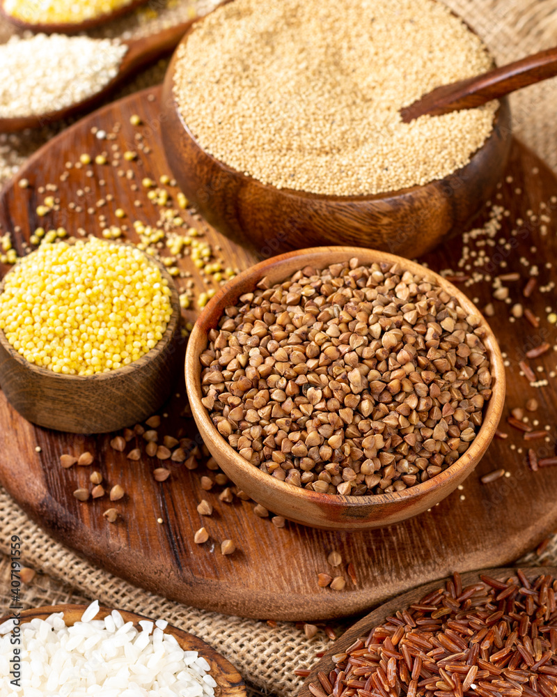White and red rice, buckwheat, amaranth seeds, corn groats, quinoa and millet in bowls on a brown wooden table. Gluten-free cereals. Closeup White and red rice, buckwheat, amaranth seeds, corn groats, quinoa and millet in bowls on a brown wooden table. Gluten-free cereals. Closeup