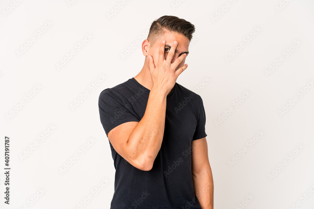 Young caucasian handsome man isolated blink at the camera through fingers, embarrassed covering face. Young caucasian handsome man isolated blink at the camera through fingers, embarrassed covering face.