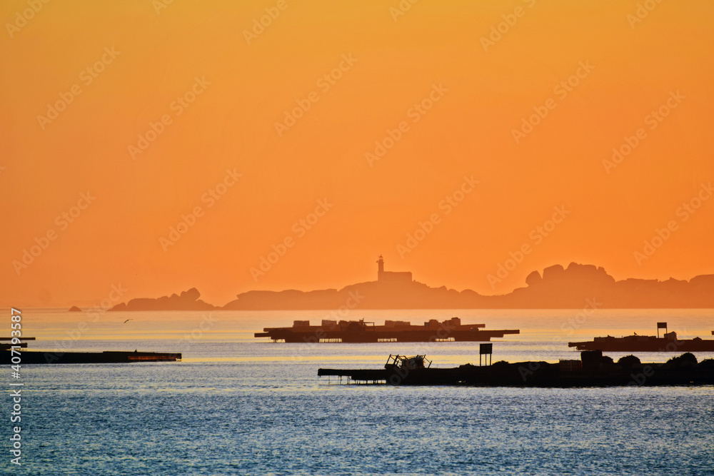 Sea landscape at dusk. Silhouettes of fishing platforms and an island with a lighthouse in the distance Sea landscape at dusk. Silhouettes of fishing platforms and an island with a lighthouse in the distance