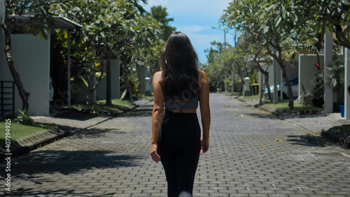 European brunette sports girl walks along an empty city street with green trees in the background alone