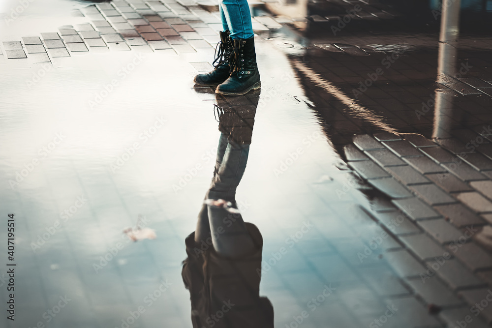 Obraz A woman in boots stands near the puddles. Reflections of the sky in puddles. Lower angle. The concept of psychology and loneliness
