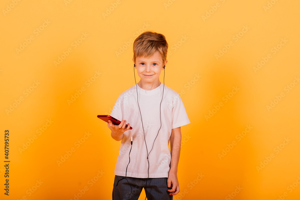 Small boy in jeans isolated on a yellow background keeps your smartphone with connected headphones Small boy in jeans isolated on a yellow background keeps your smartphone with connected headphones