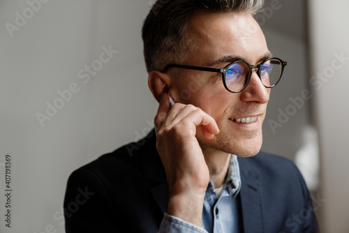 Pleased grey man smiling and using wireless earphones while working