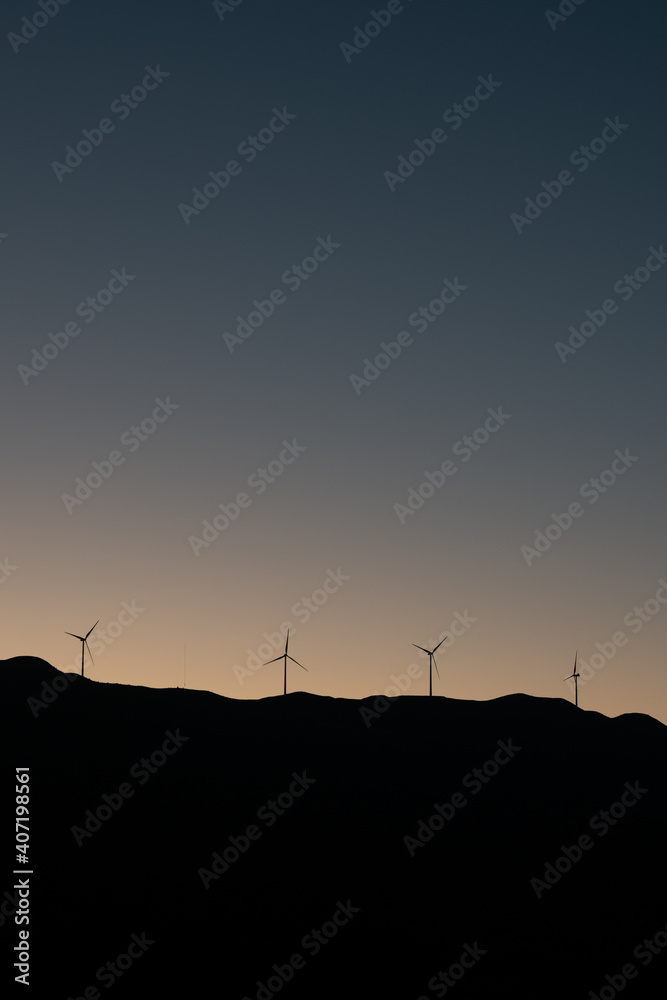 The wind turbines on top of hill at sunset, backlit.