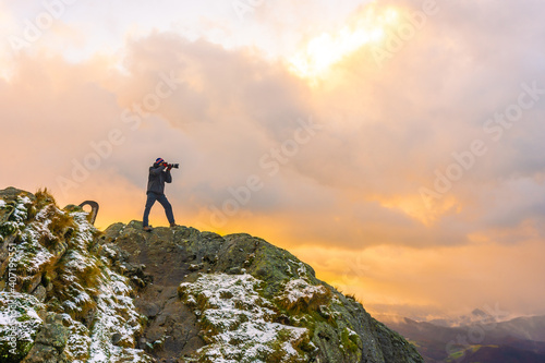 A photographer on top of the mountain in the snowy winter orange sunset, on Mount Peñas de Aya in the town of Oiartzun near San Sebastián, Gipuzkoa. Basque Country