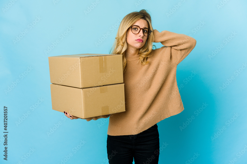 Young blonde caucasian woman holding boxes to move being shocked, she has remembered important meeting.