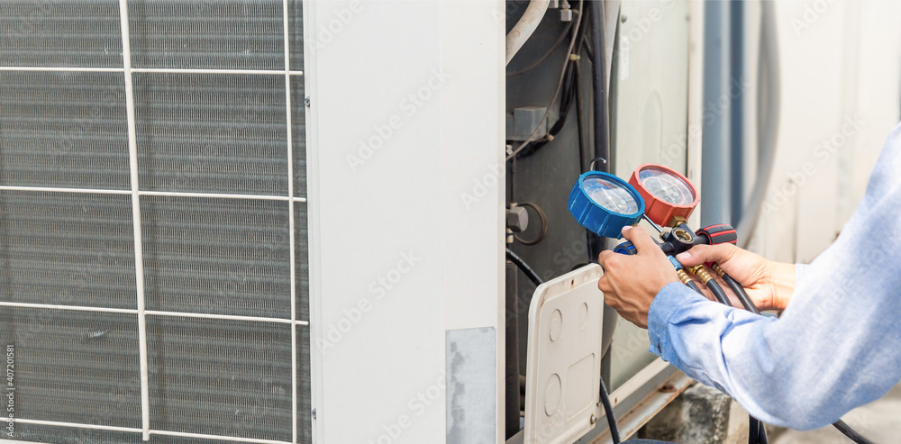 Air repair mechanic using measuring equipment for filling industrial factory air conditioners and checking maintenance outdoor air compressor unit.