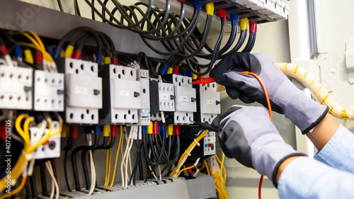 Electrical engineer using digital multi-meter measuring equipment to checking electric current voltage at circuit breaker and cable wiring system in main power distribution board.