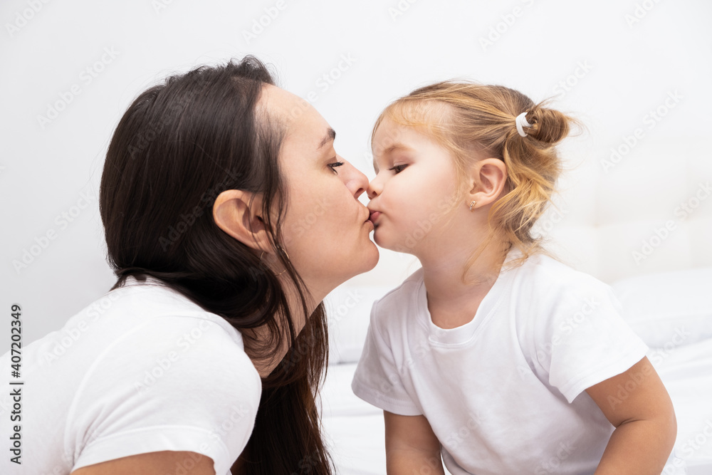adult brunet mother kissing her little blond daughter, white background. adult brunet mother kissing her little blond daughter, white background.
