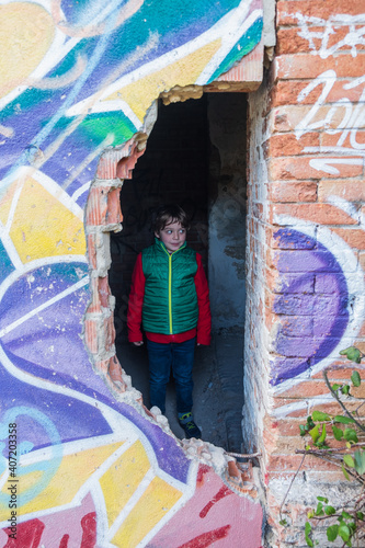 Five year old boy in a red jacket and green vest, enters an abandoned house