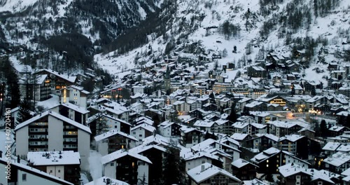 Cityscape of the Swiss village of Zermatt in Valais in winter, at dawn with snow and illuminations. The Matterhorn and the Alpine mountain range in the background.