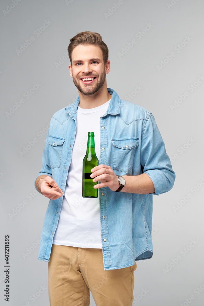 Young Man holding wearing jeans shirt holding Bottle of beer standing over Grey Background Young Man holding wearing jeans shirt holding Bottle of beer standing over Grey Background