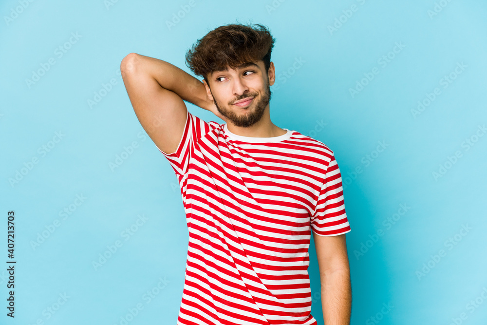 Young arab man on blue background touching back of head, thinking and making a choice. Young arab man on blue background touching back of head, thinking and making a choice.