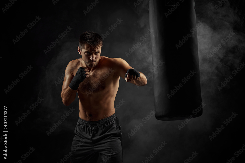 Male boxer training defense and attacks in boxing bag on black background