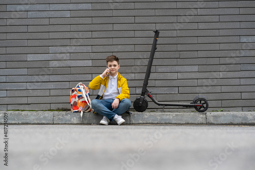 Wallpaper Mural Modern teenager with backpack and electric scooter sitting on the sidewalk and talking on the phone Torontodigital.ca