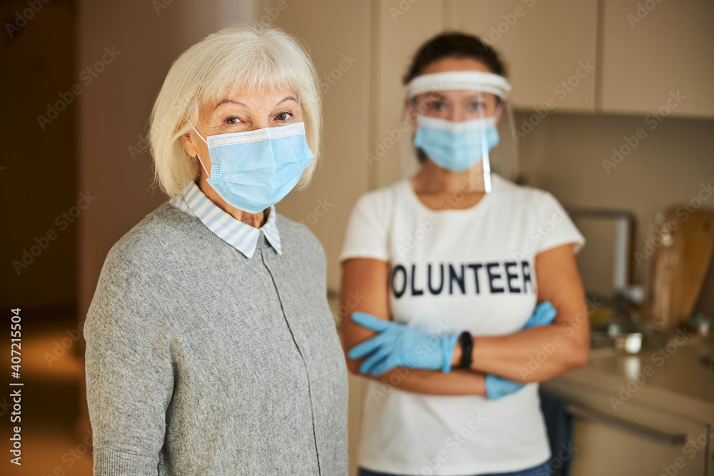 Volunteer in latex gloves standing behind a senior lady