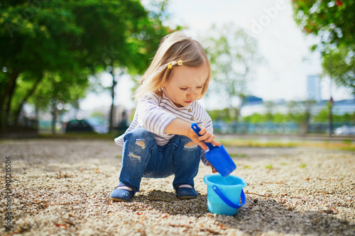Adorable toddler girl playing with bucket and shovel, making mudpies and gathering small stones © Ekaterina Pokrovsky